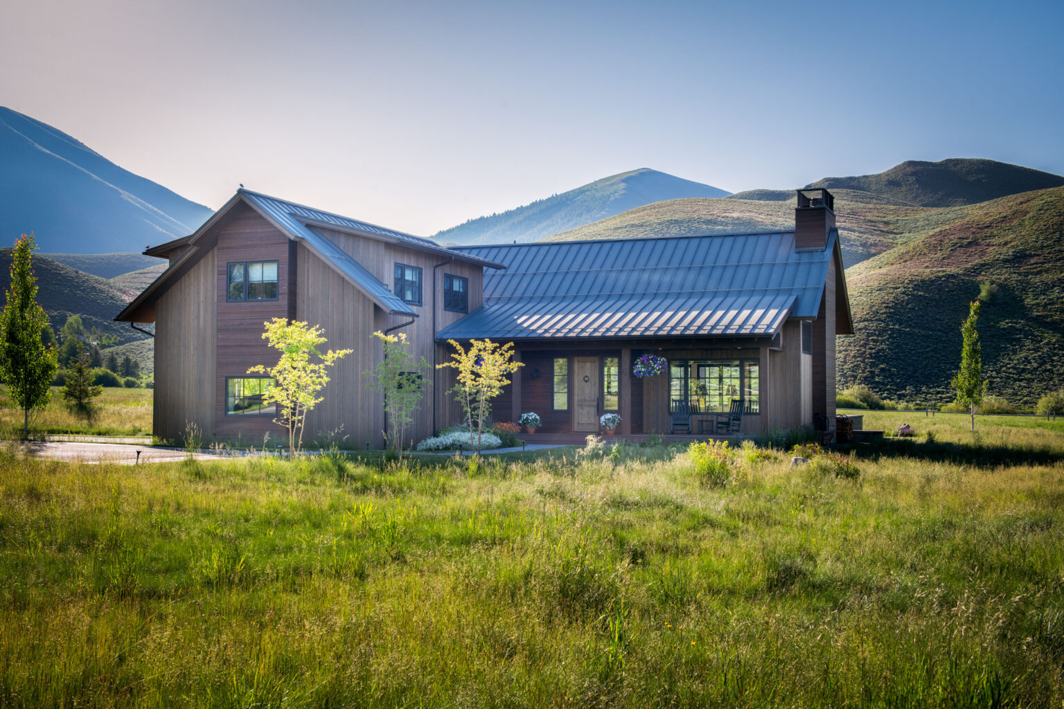 Photo of a house in a green field with mountains in the background.