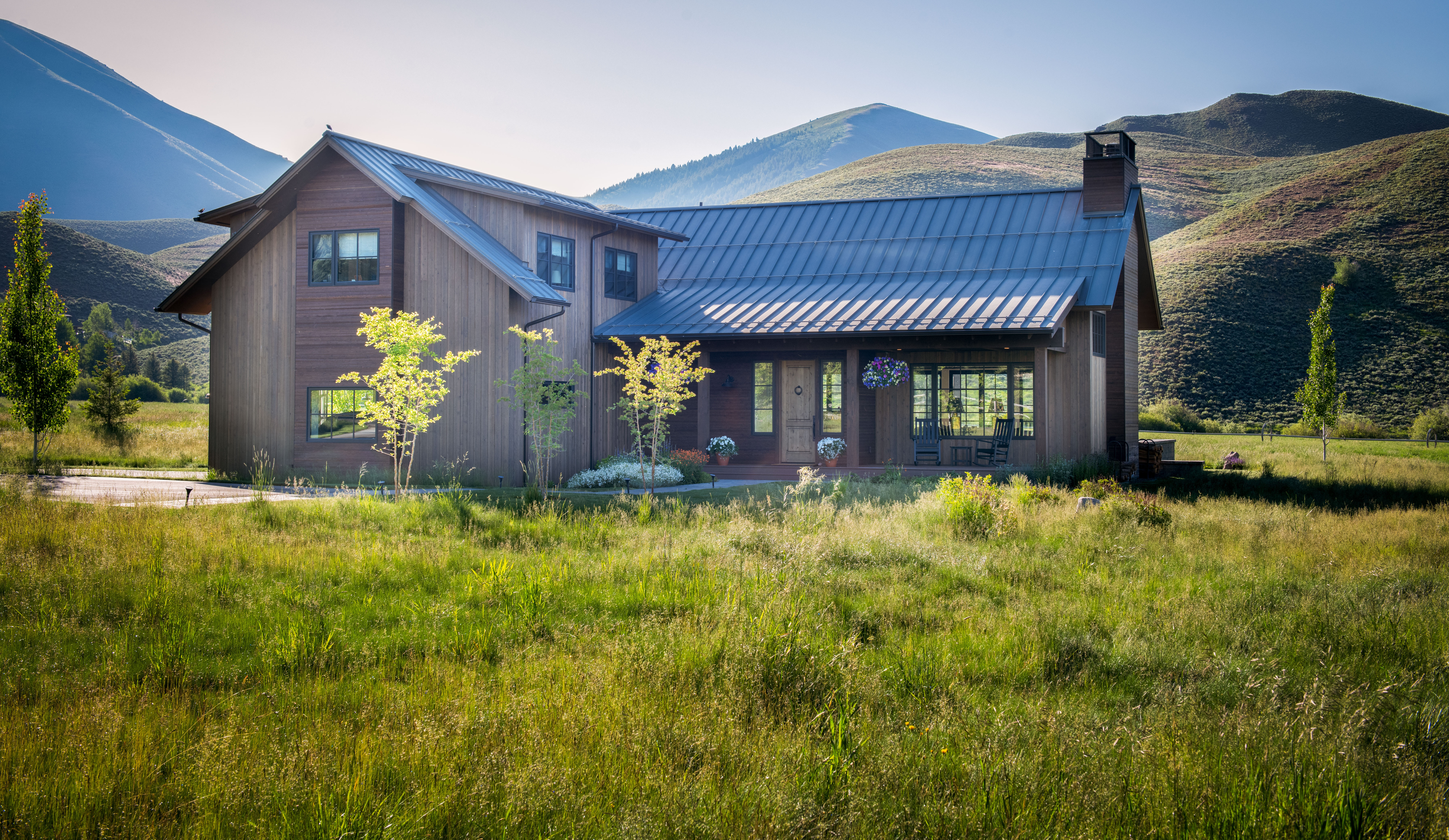 Photo of a house in a green field with mountains in the background.